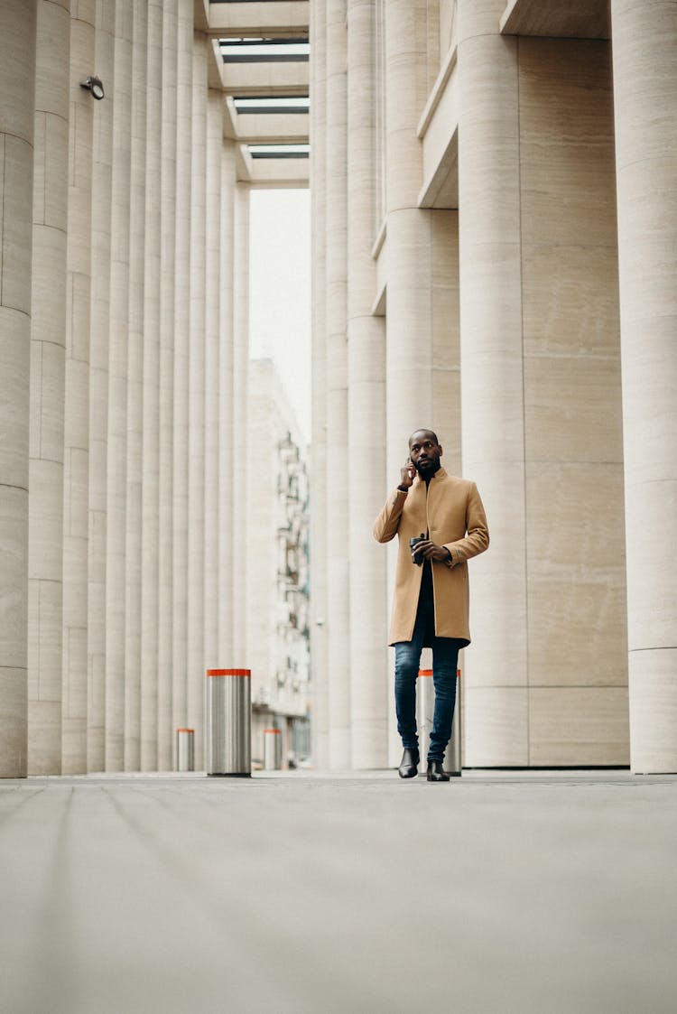 Man In Brown Coat Standing Beside Concrete Wall