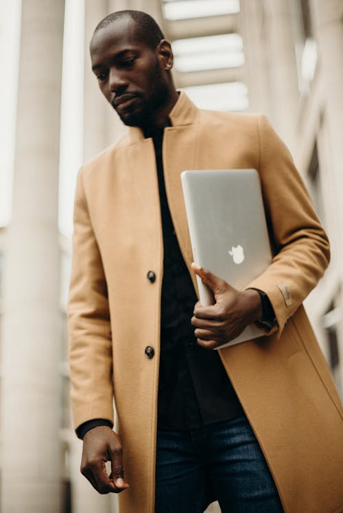 Free Man Wearing Orange Trench Coat Holding Silver Macbook Pro Stock Photo