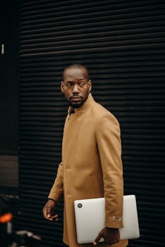 一位时髦男士手拿笔记本电脑，穿行于城市街景之中，完美诠释了科技与生活方式的融合主题