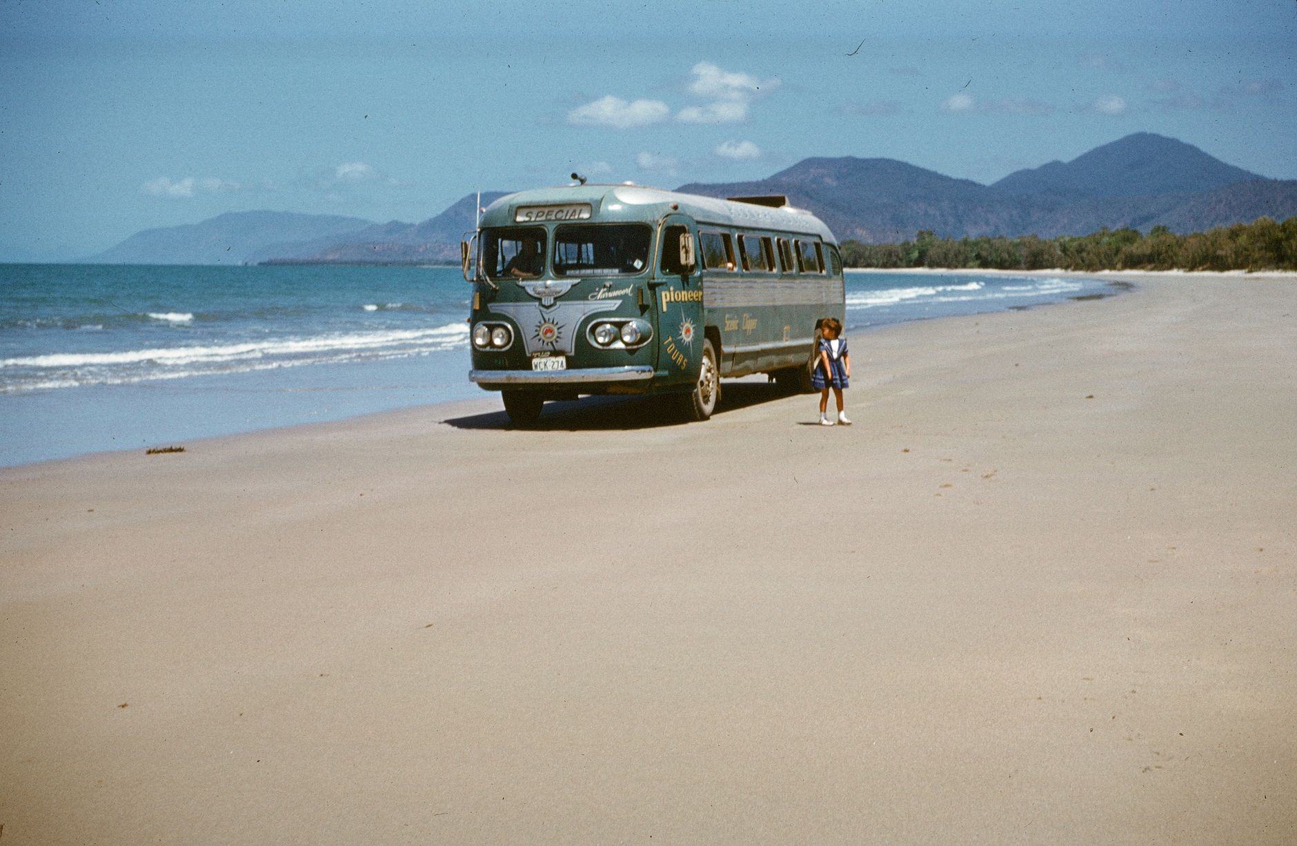 A nostalgic scene of a vintage bus and a child on a beautiful Queensland beach.