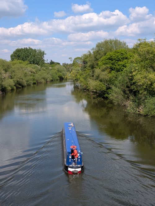 Free A blue canal boat glides through a lush green river surrounded by trees on a clear day. Stock Photo