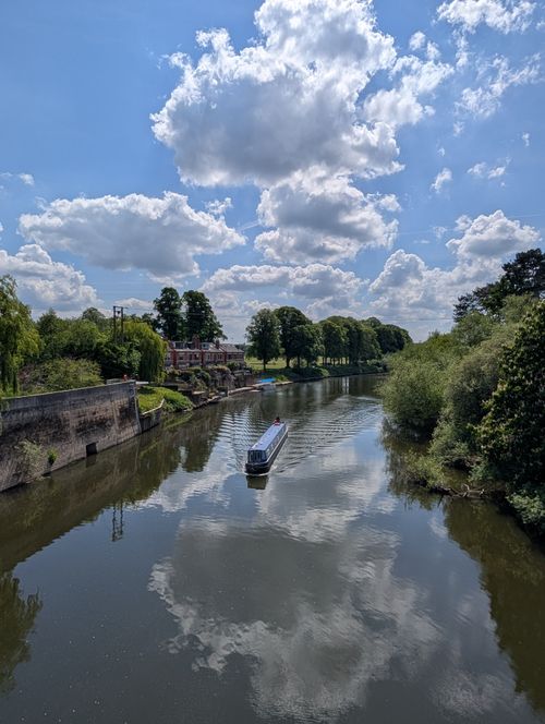 Free Serene river reflecting sky and clouds, featuring a blue boat on a calm sunny day. Stock Photo