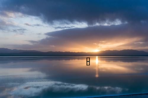 Free Beautiful sunrise over a calm lake with mirrored reflections and mountains in the background. Stock Photo
