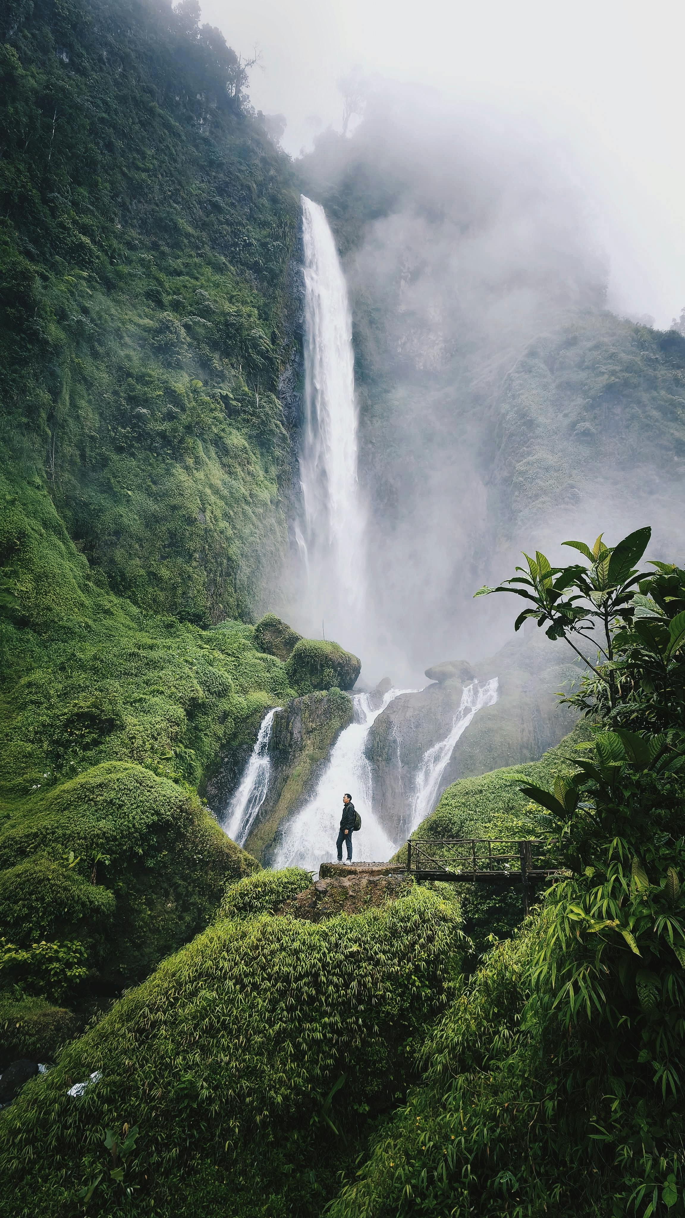 Adult exploring lush misty waterfall landscape in Indonesia. Adventure awaits.