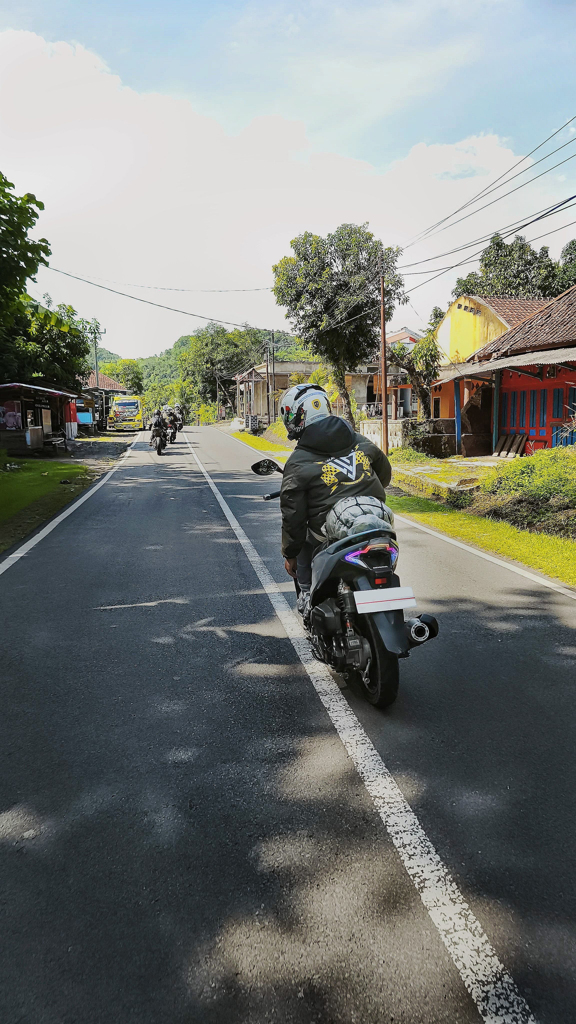 A group of motorcyclists enjoying a sunny day ride on a rural road in Indonesia.