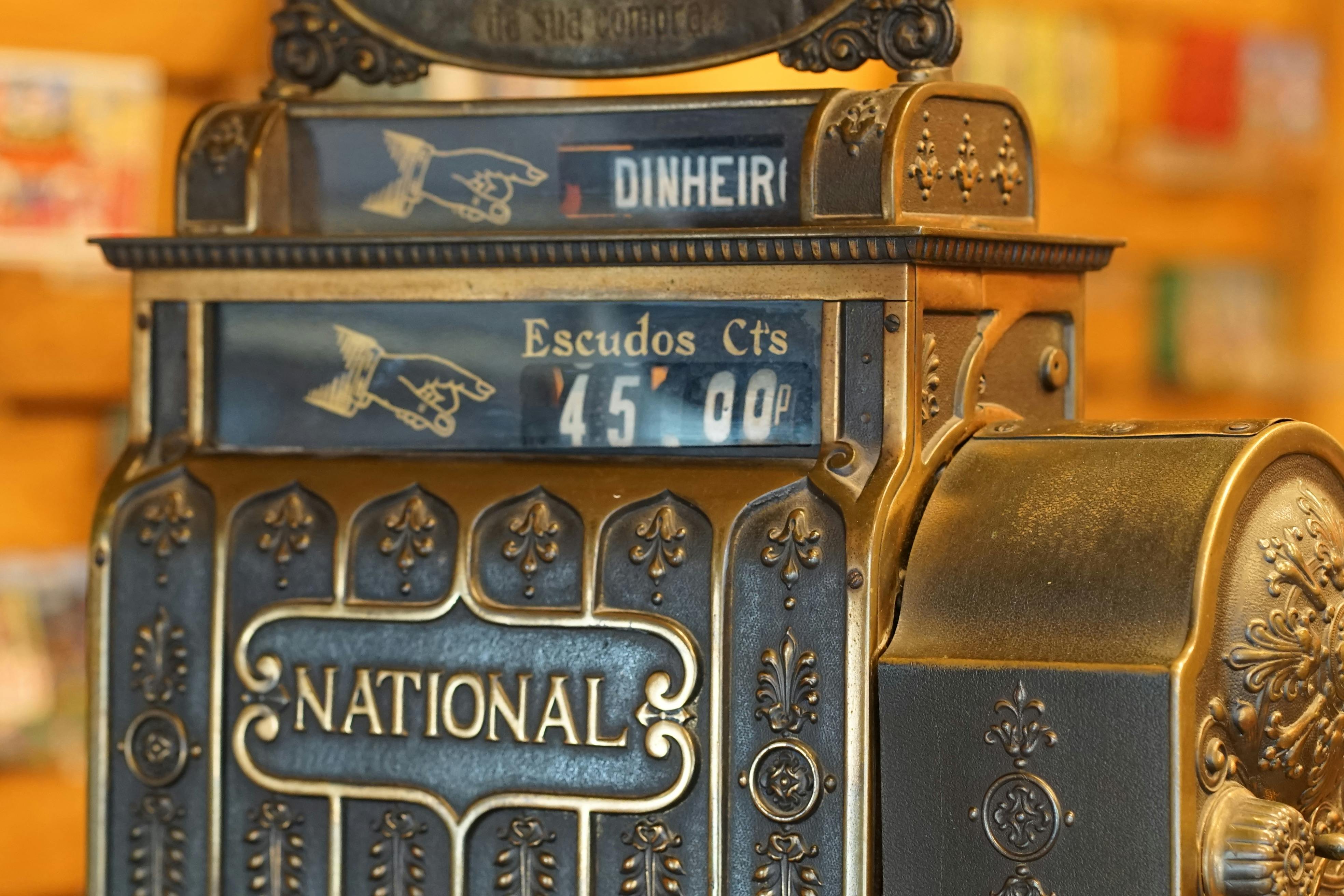 Close-up of ornate vintage brass cash register displaying price in escudos.