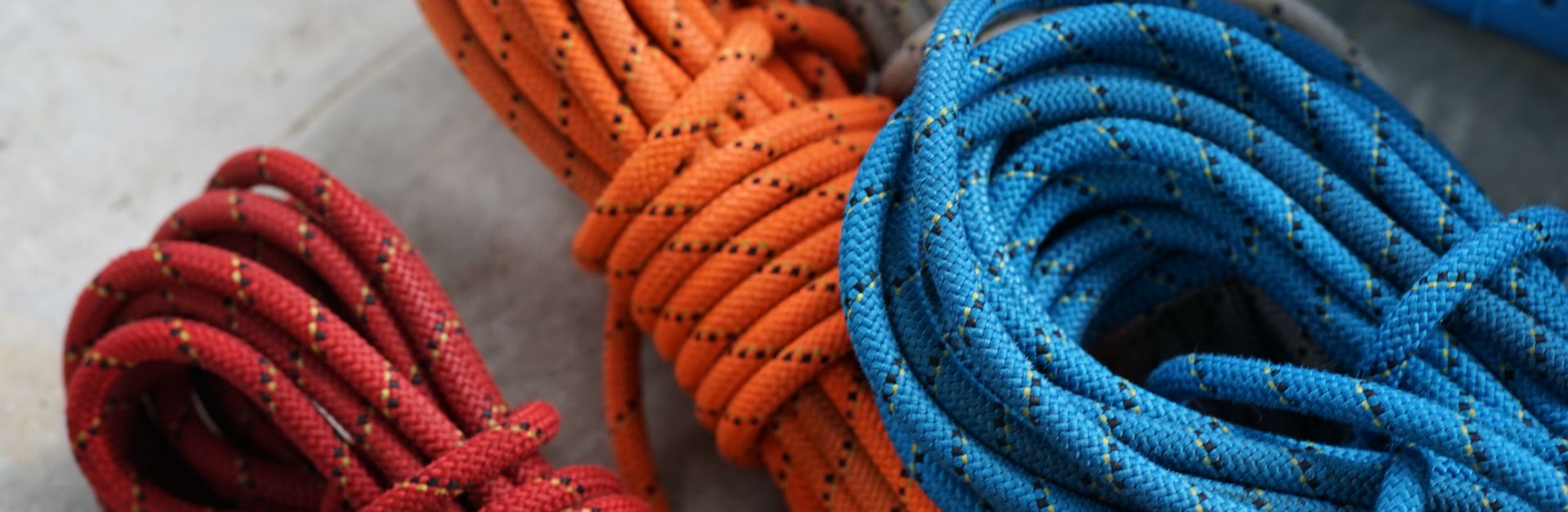 Vibrant red, orange, and blue climbing ropes coiled on concrete surface.