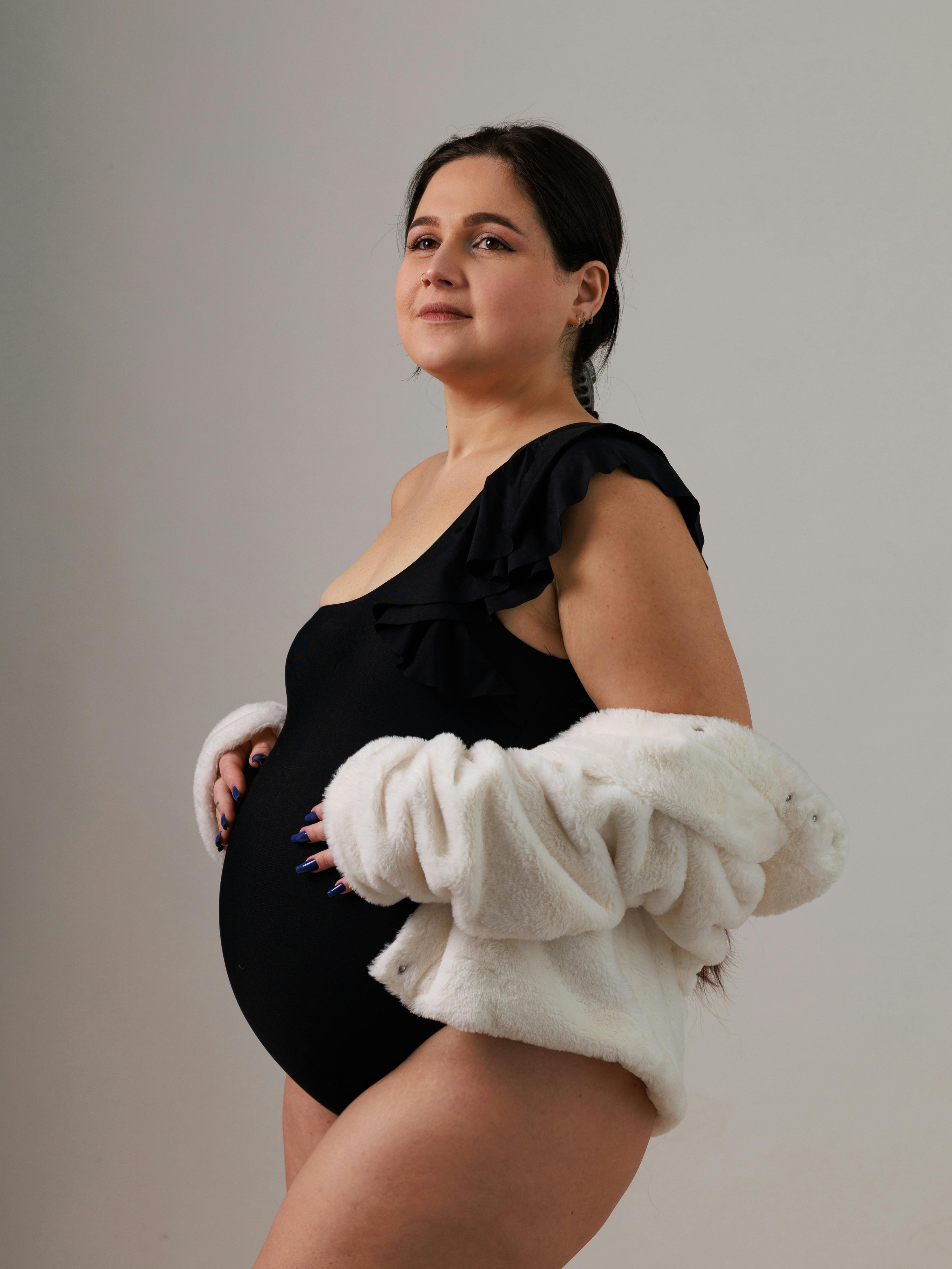 Confident pregnant woman in a black swimsuit draped with white fur. Stylish and poised.