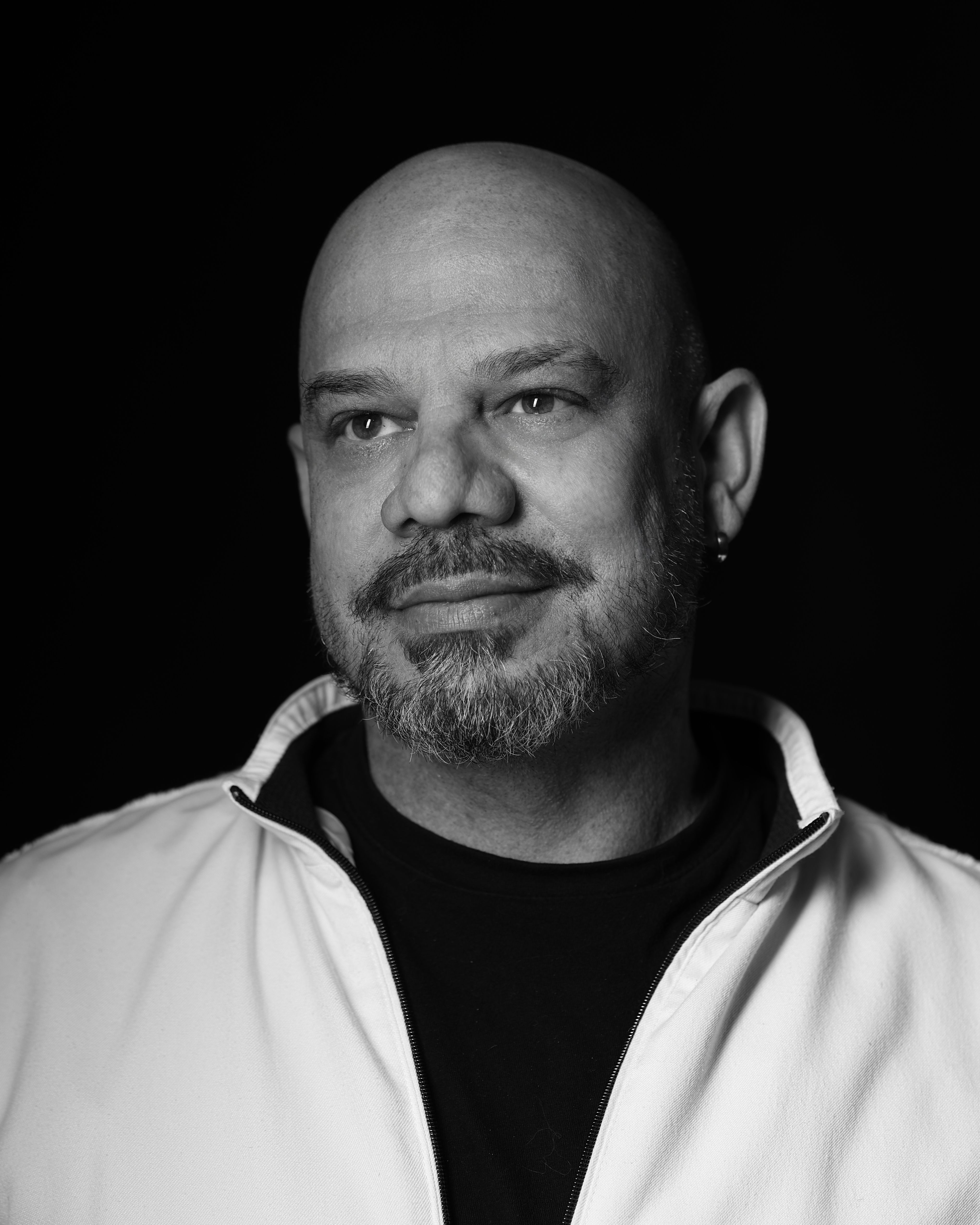 A professional black and white portrait of a man in a white jacket against a dark background.