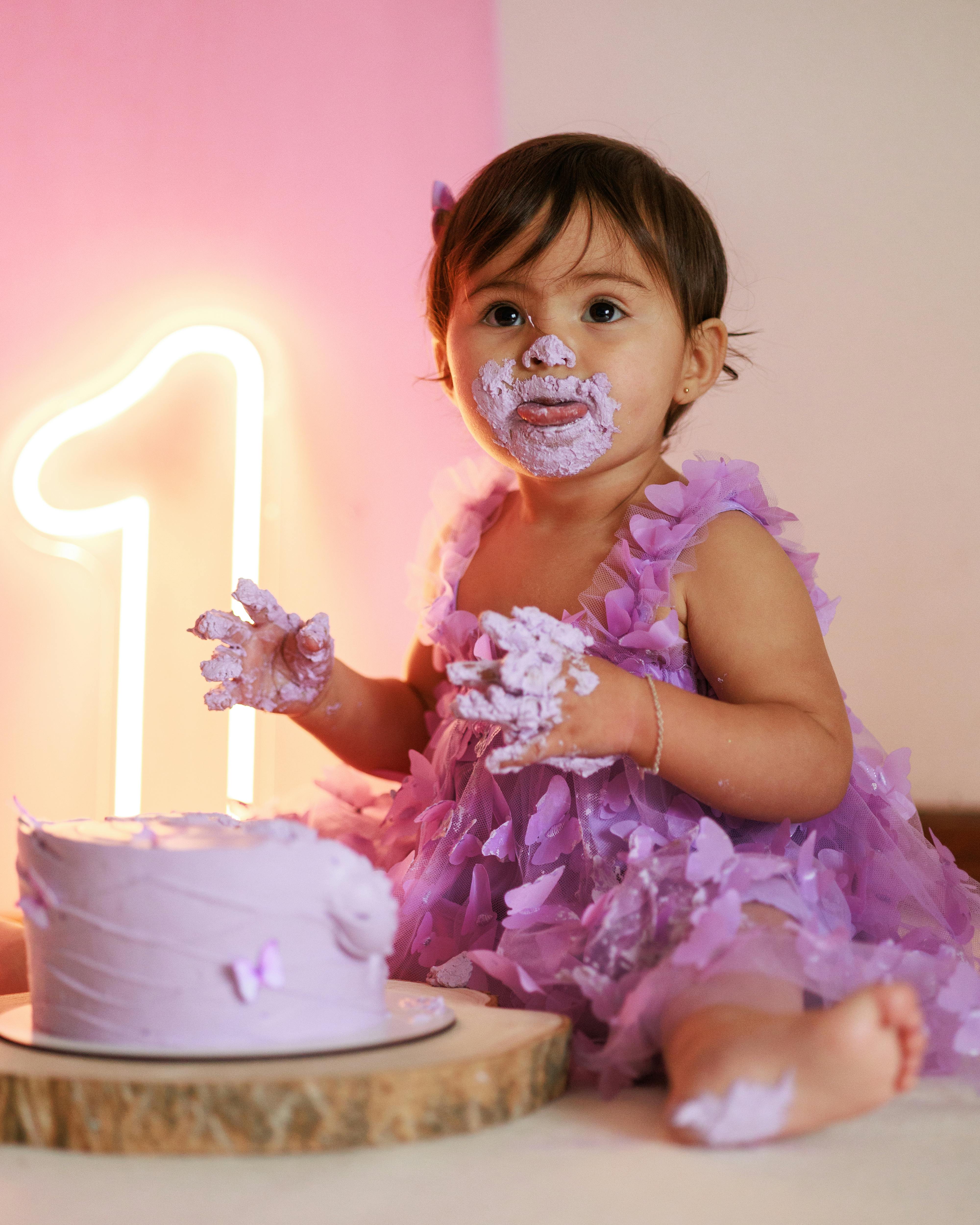 Cute baby in purple dress enjoying a cake smash for her first birthday.