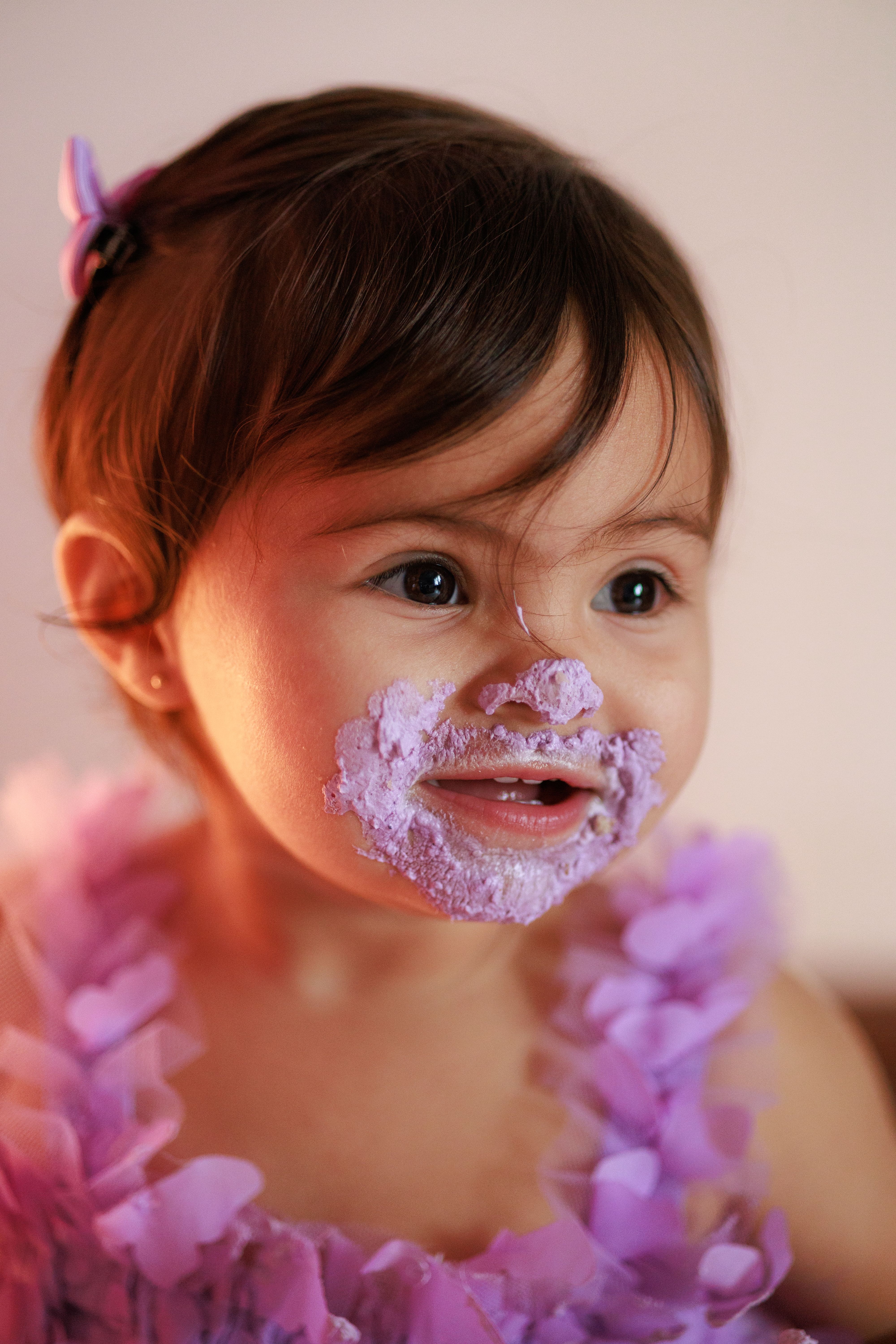 Cute baby with purple cake on face, joyous expression indoors.
