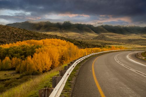 Free Curved road through mountains with vibrant autumn trees and dramatic clouds. Stock Photo