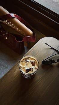 Stylish iced coffee on a wooden table by a window, perfect for a serene cafe experience.