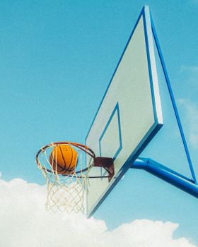 Basketball caught mid-air as it goes through the hoop on a clear sunny day.
