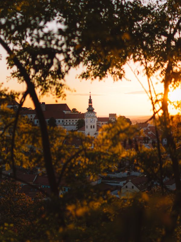 A historic church tower seen through trees during a vibrant sunset, creating a serene and picturesque landscape.