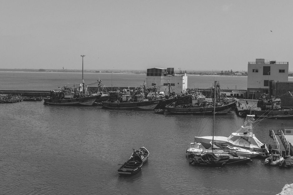 Scenic view of the fishing port in El Jadida, Morocco, showcasing boats and waterfront buildings in black and white.