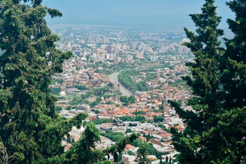 Free Panoramic aerial view of Tbilisi, showcasing diverse architecture and vibrant landscape framed by trees. Stock Photo