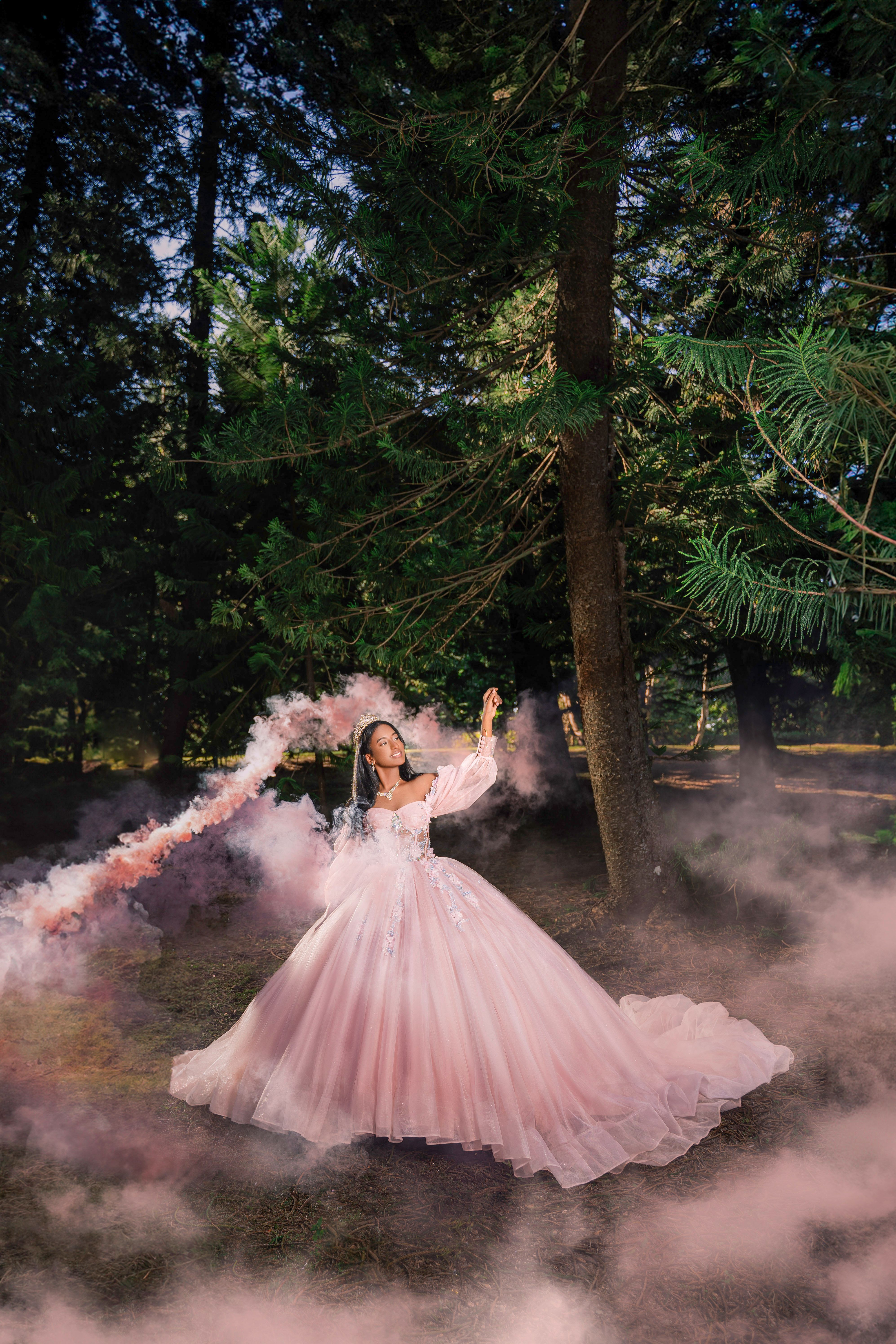 Elegant woman in pink gown stands gracefully in a misty forest, exuding fairy-tale magic.