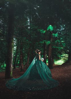 Woman in a sparkling green gown in a mystical forest setting. Magical and elegant vibe.