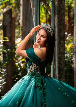 Young woman in a glamorous green dress and crown posing gracefully outdoors.