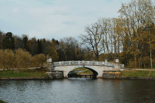 Free A picturesque stone bridge arches gracefully over a serene river surrounded by autumn trees. Stock Photo