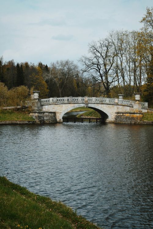 Free A serene view of a historic stone bridge over a calm river, surrounded by early spring trees. Stock Photo