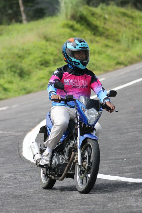 Free Adult riding a motorcycle on a winding road in Bicol, Philippines with a vibrant landscape background. Stock Photo