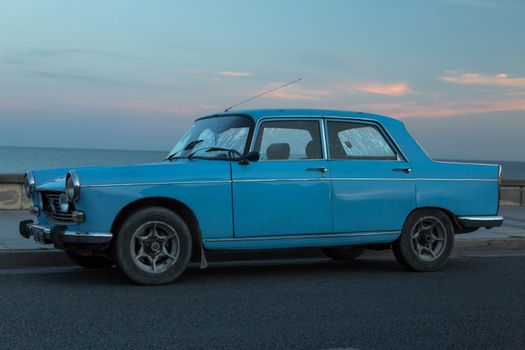 Classic blue car parked by the ocean during twilight in Mar del Plata, Argentina.