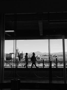 Black and white photo of silhouettes walking inside León airport with construction outside.