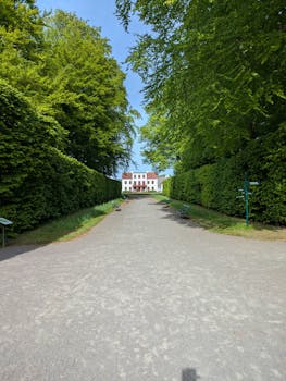 A picturesque white mansion framed by vibrant green hedges under a clear blue sky.