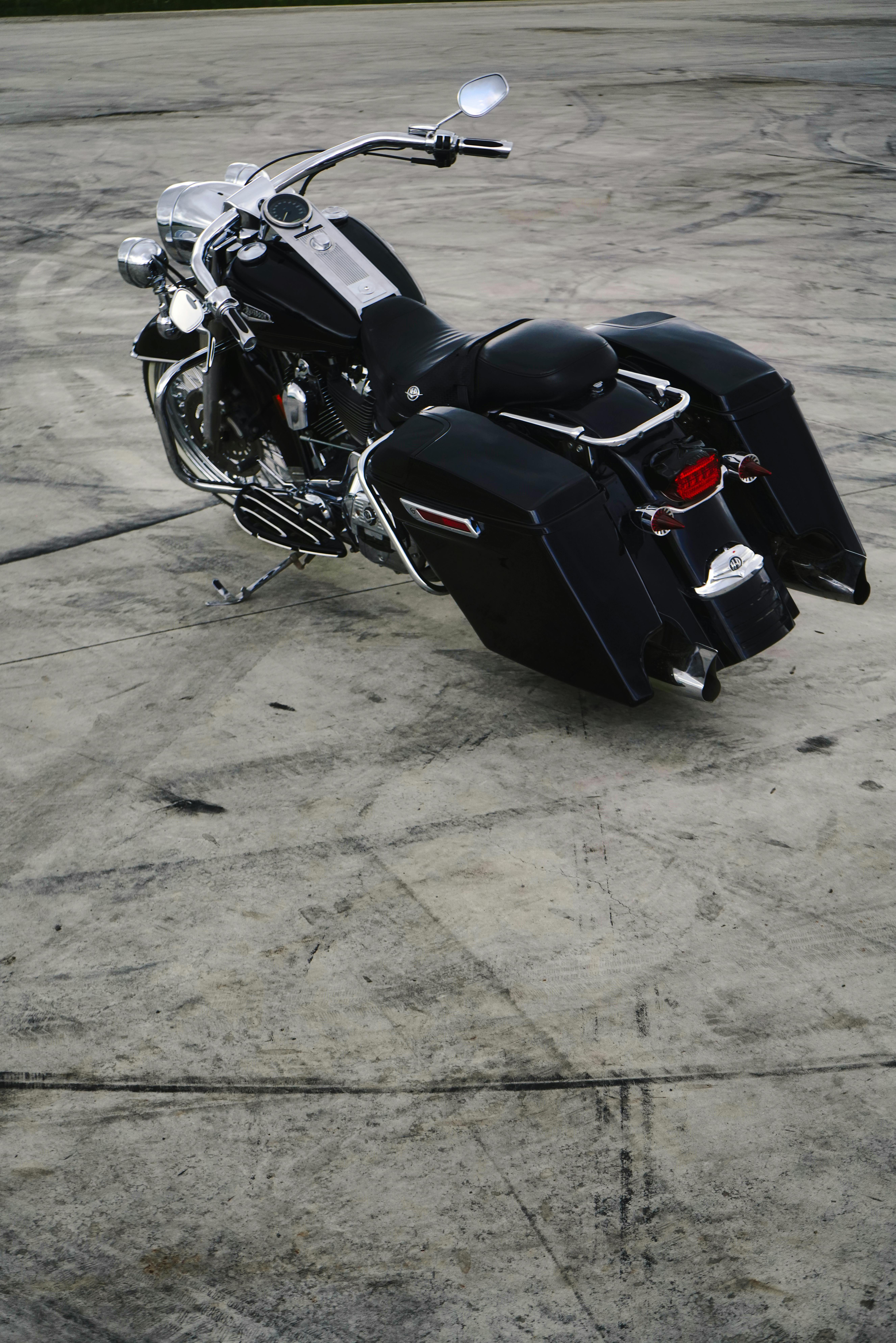 Free A sleek black motorcycle rests on an open concrete area, showcasing its shiny chrome details. Stock Photo