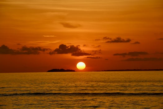 A tranquil sunset over the ocean with a vivid orange sky and clouds.