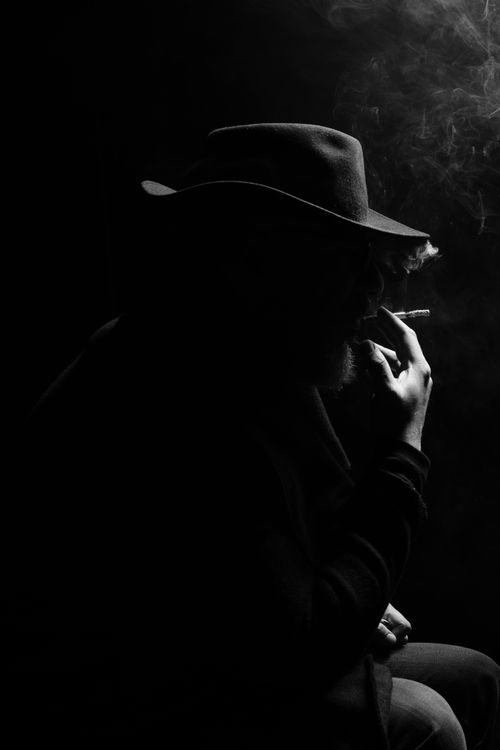Free Artistic silhouette of a man in a hat smoking, captured in moody low light and black and white. Stock Photo