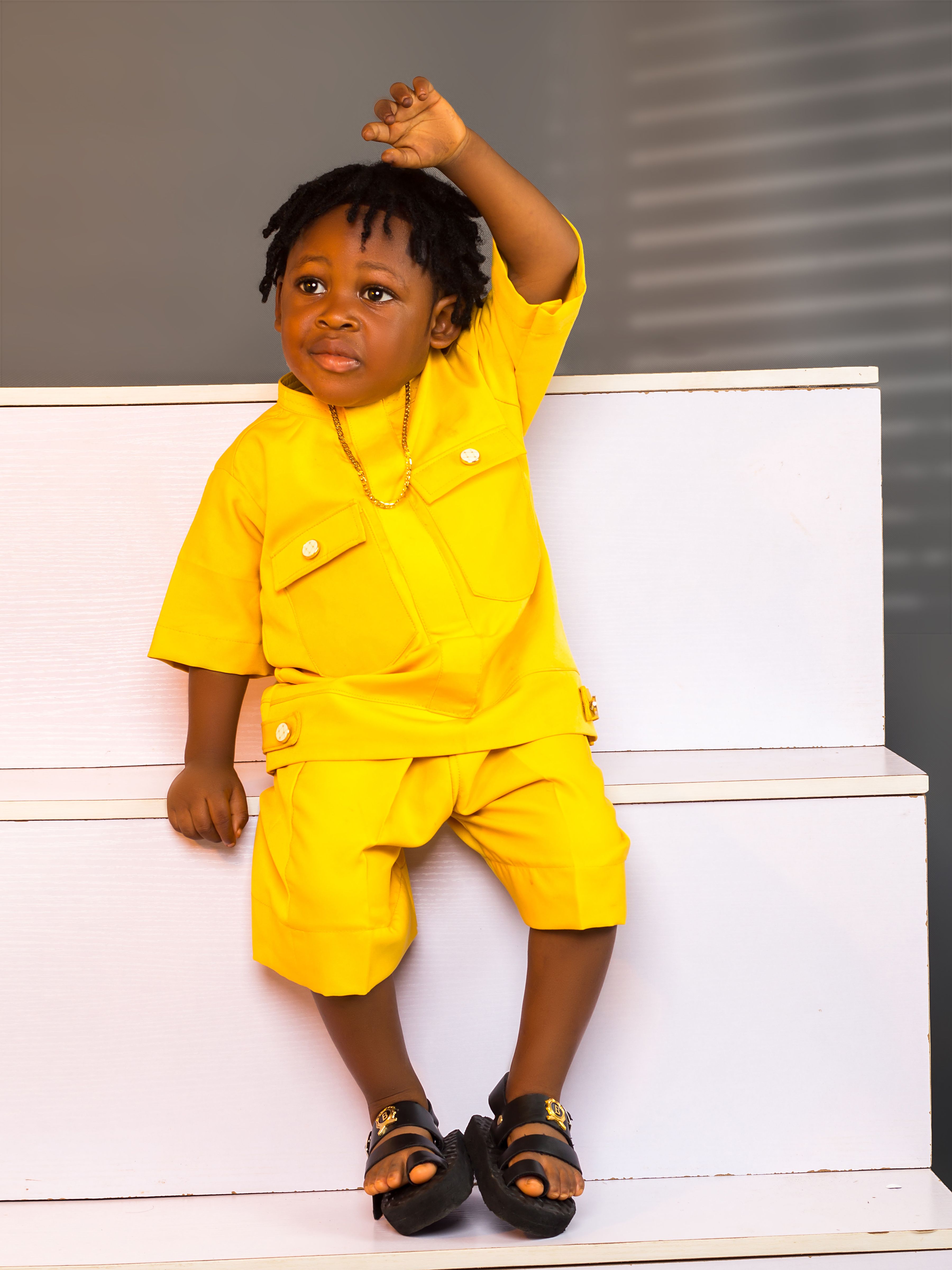 Cute child dressed in vibrant yellow sitting on white steps indoors.
