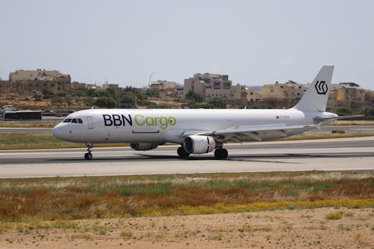 A BBN Cargo airplane taxiing on a runway on a sunny day with buildings in the background.
