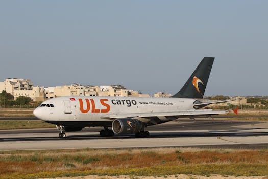 A ULS Cargo aircraft taxiing on a sunny airport runway with buildings in the background.