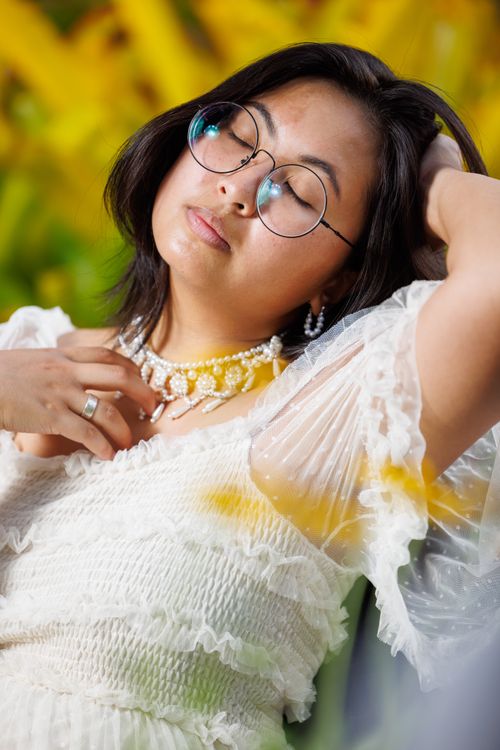 Free Elegant woman with glasses in a white dress relaxing against a vibrant yellow background. Stock Photo