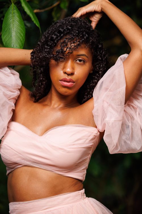 Free Stylish woman in pink with natural curls posing outdoors with leafy background. Stock Photo