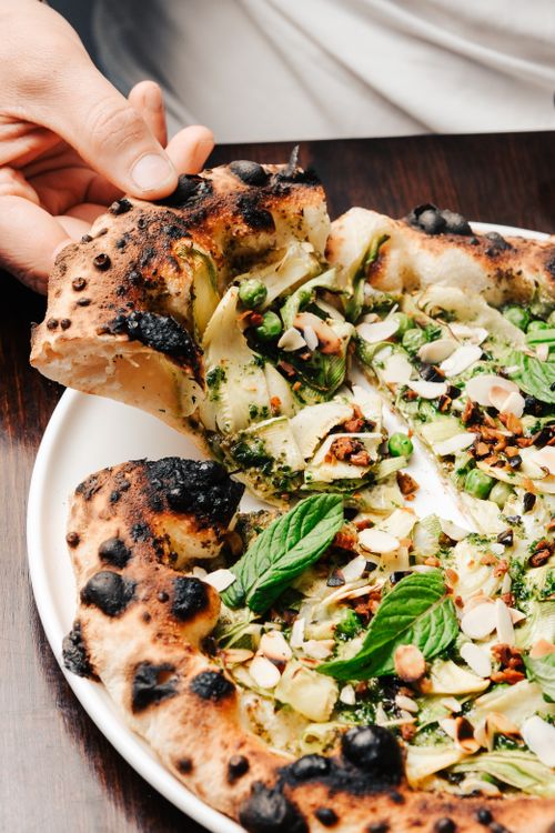 Free Close-up of a gourmet artisanal pizza topped with greens, nuts, and herbs. Stock Photo