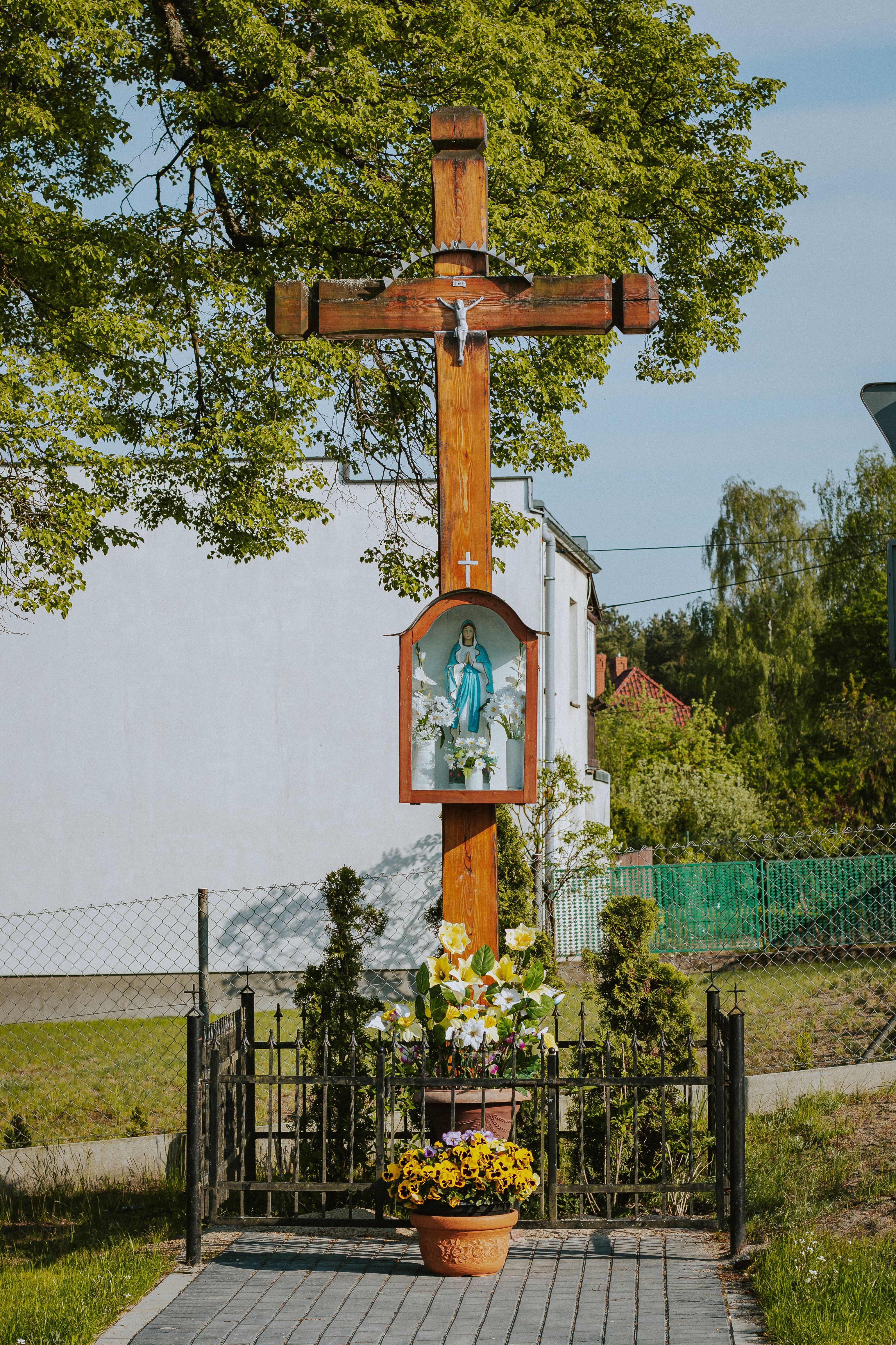 Outdoor wooden crucifix with Holy Mary image and floral arrangements in Ocypel, Poland.