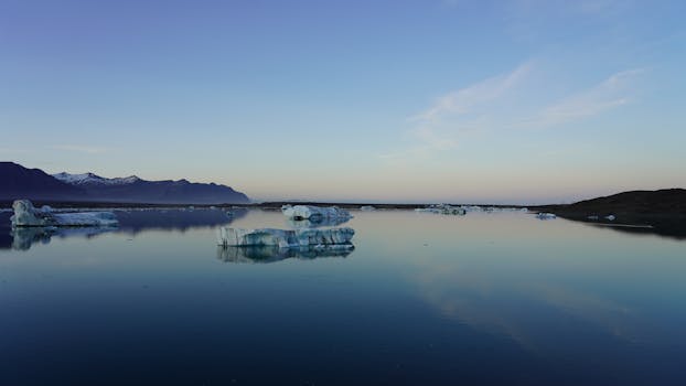 Serene view of icebergs floating in an Icelandic lagoon during sunset with clear skies.