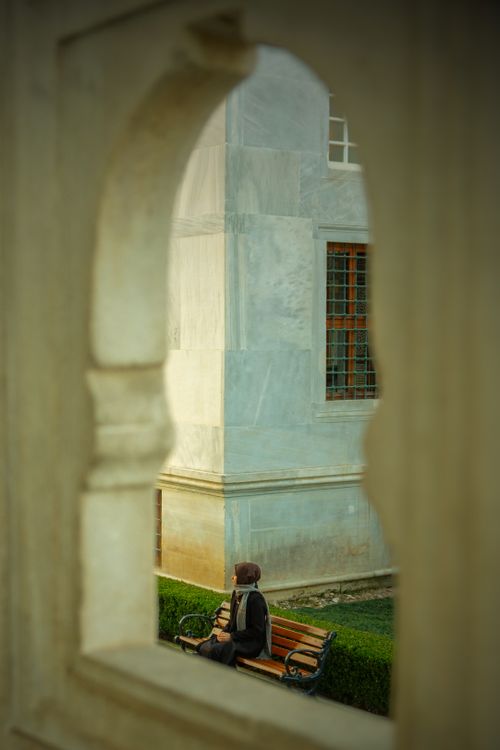 Free A person sits on a bench in a park in İstanbul, framed by architectural arches. Stock Photo