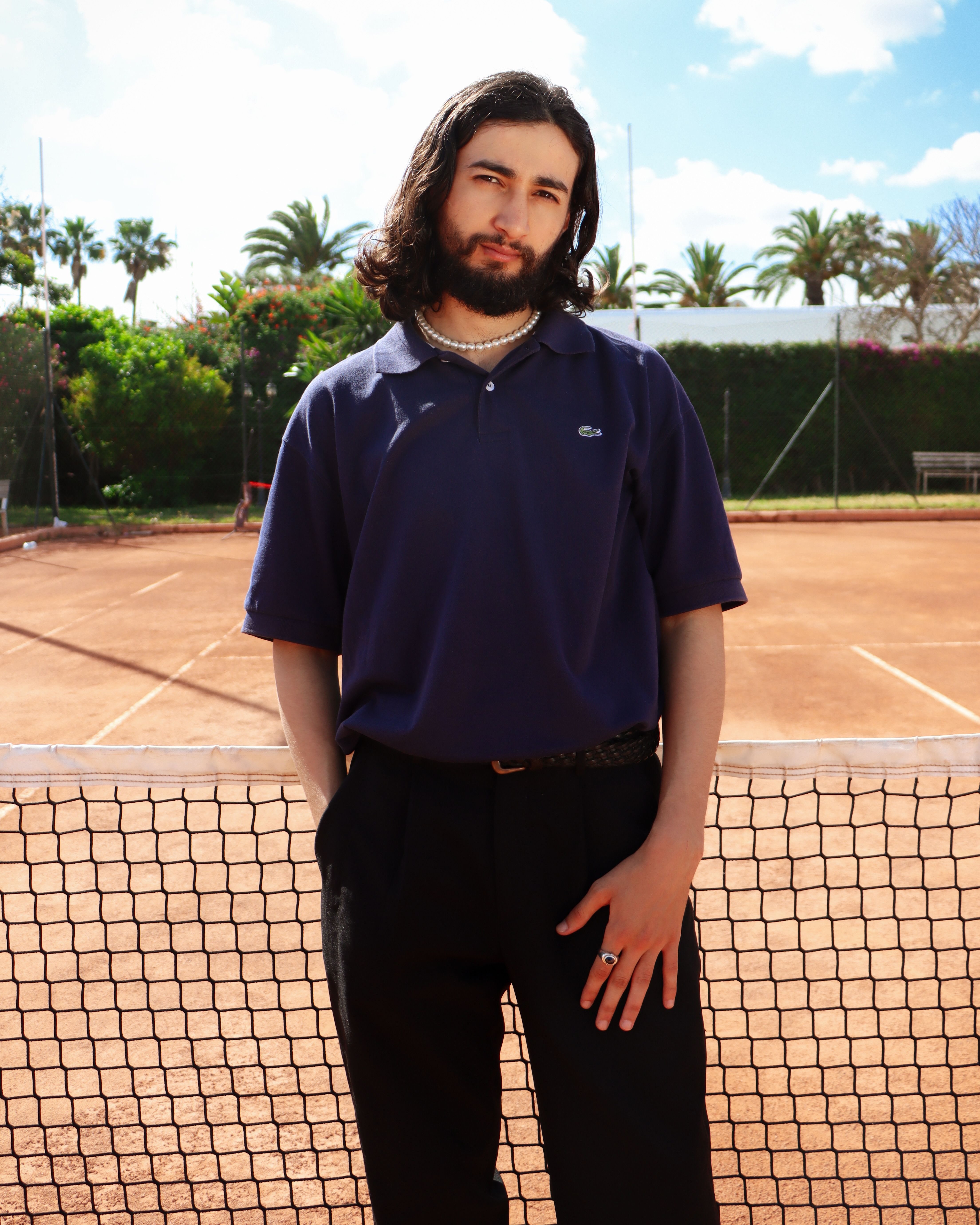A man poses confidently on a tennis court under a clear sky in Casablanca, Morocco.