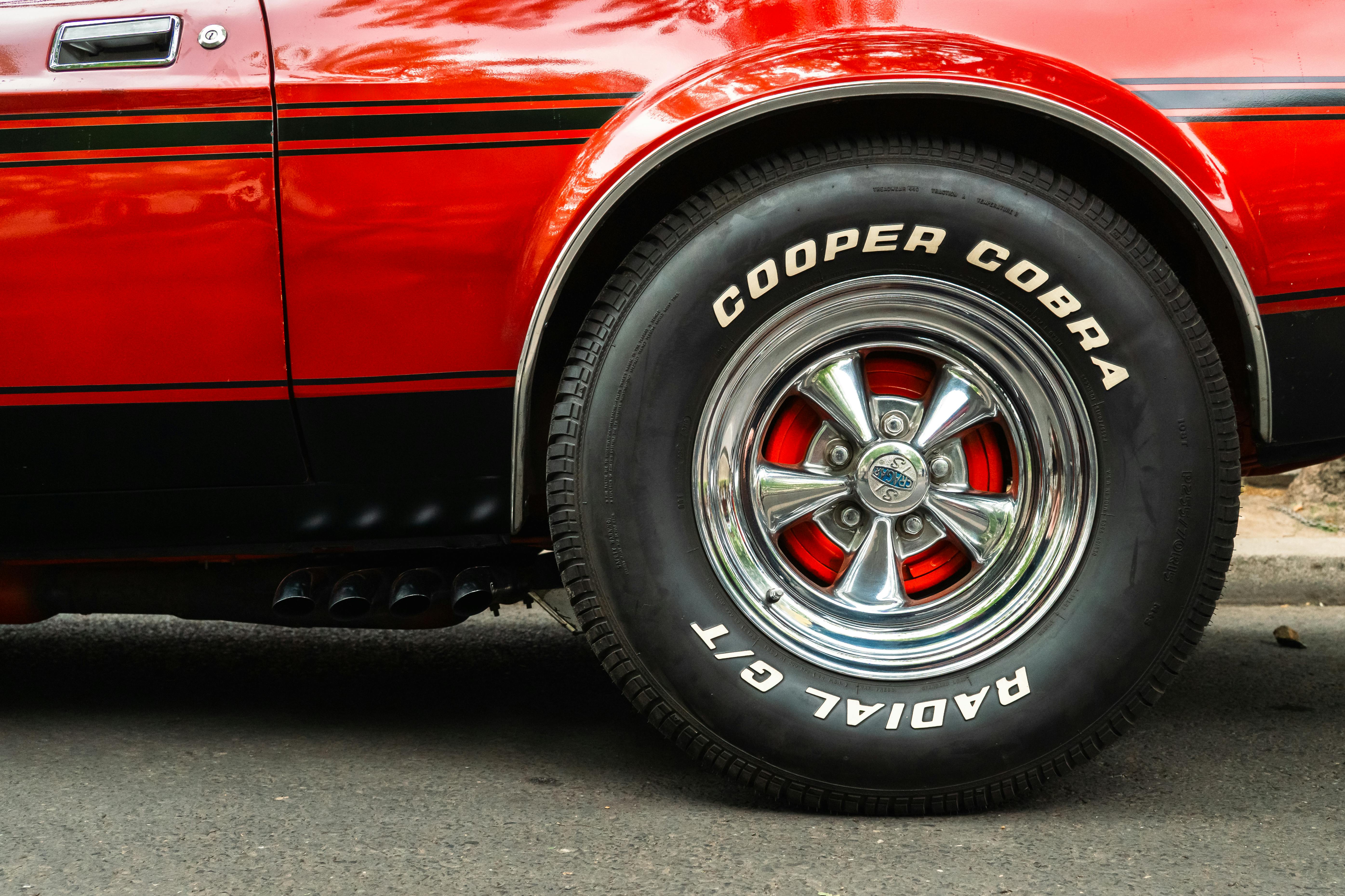 Detailed view of a classic red car's wheel featuring Cooper Cobra GT radial tires, showing automotive style.