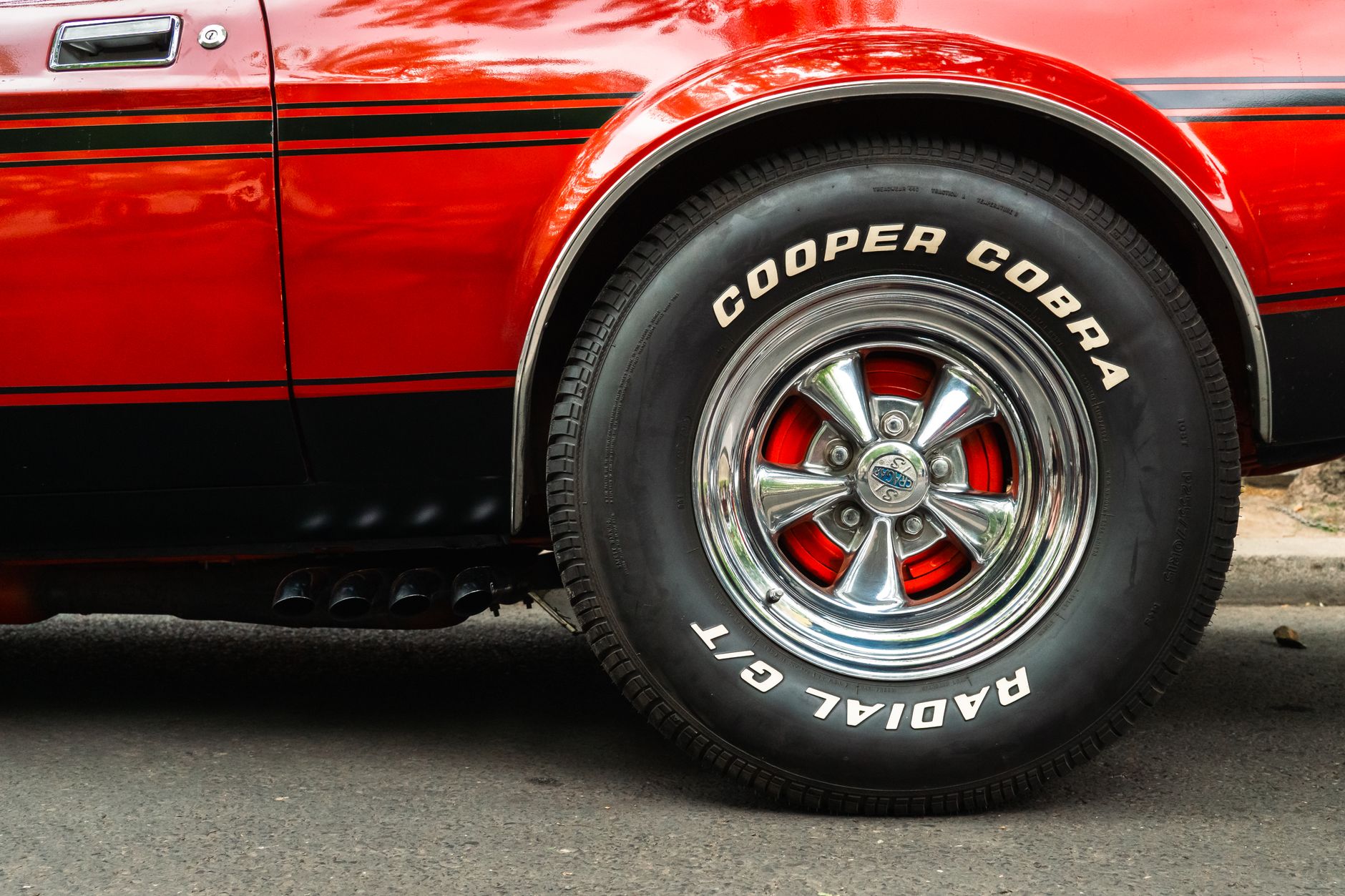Detailed view of a classic red car's wheel featuring Cooper Cobra GT radial tires, showing automotive style.