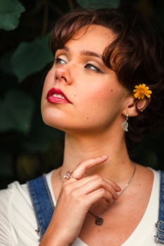 Close-up of a young woman with a yellow flower in her hair, gazing upwards thoughtfully.
