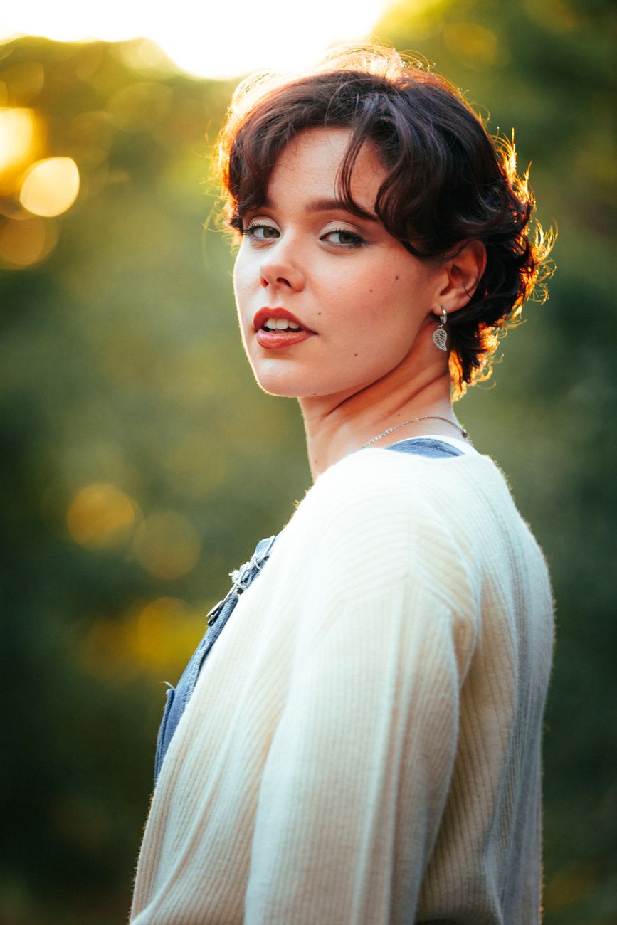 A young woman poses outdoors with soft golden light creating a warm and serene atmosphere.