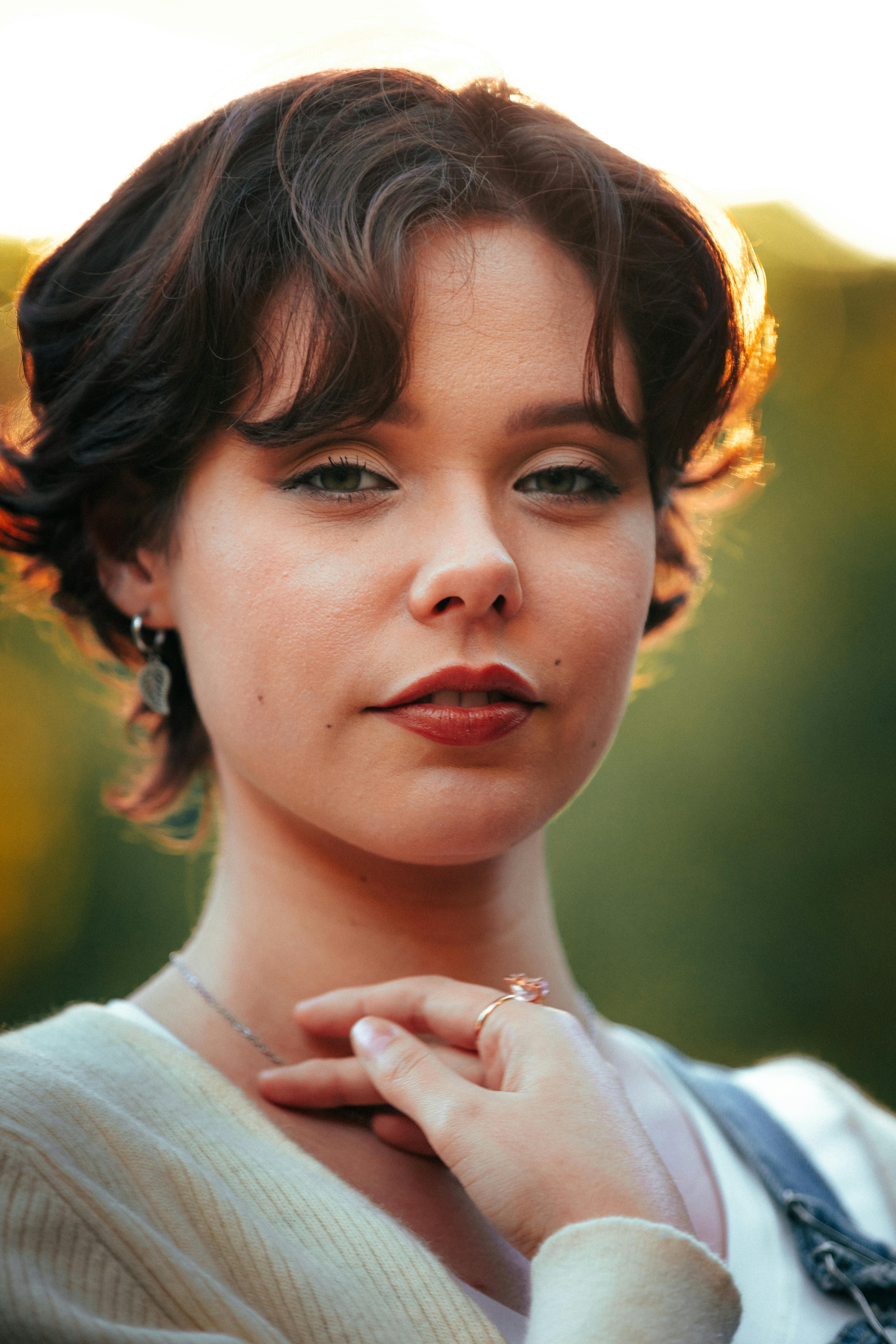 Captivating portrait of a young woman with short hair against a soft, warm sunset backdrop.