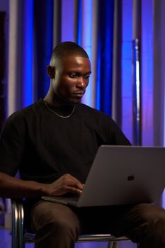 Focused man working on a laptop in a room with blue accent lighting.