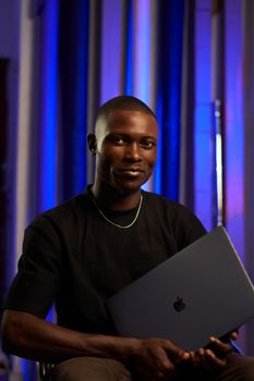 Portrait of a confident man holding a laptop, set against a stylish studio backdrop.